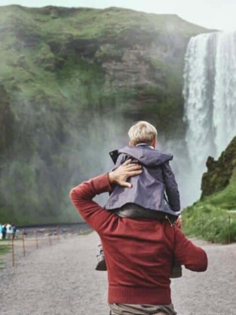 Father with son on his shoulders walking towards Skogafoss waterfall