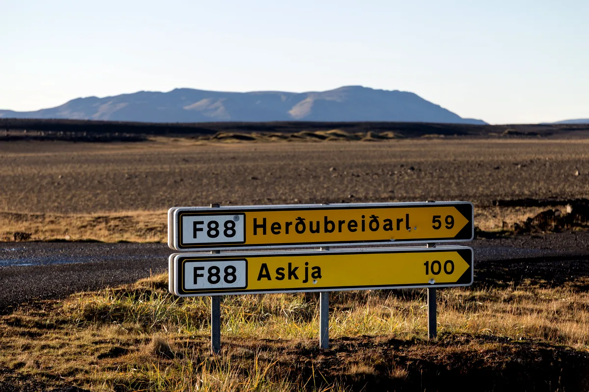A road sign in Iceland indicating directions to Herðubreiðarl and Askja along the F88 route, with a barren landscape and distant mountains in the background.